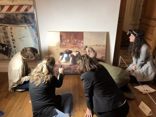 A group of five people sitting on the floor looking intently at an artwork depicting iconic paintings of Western art history.
